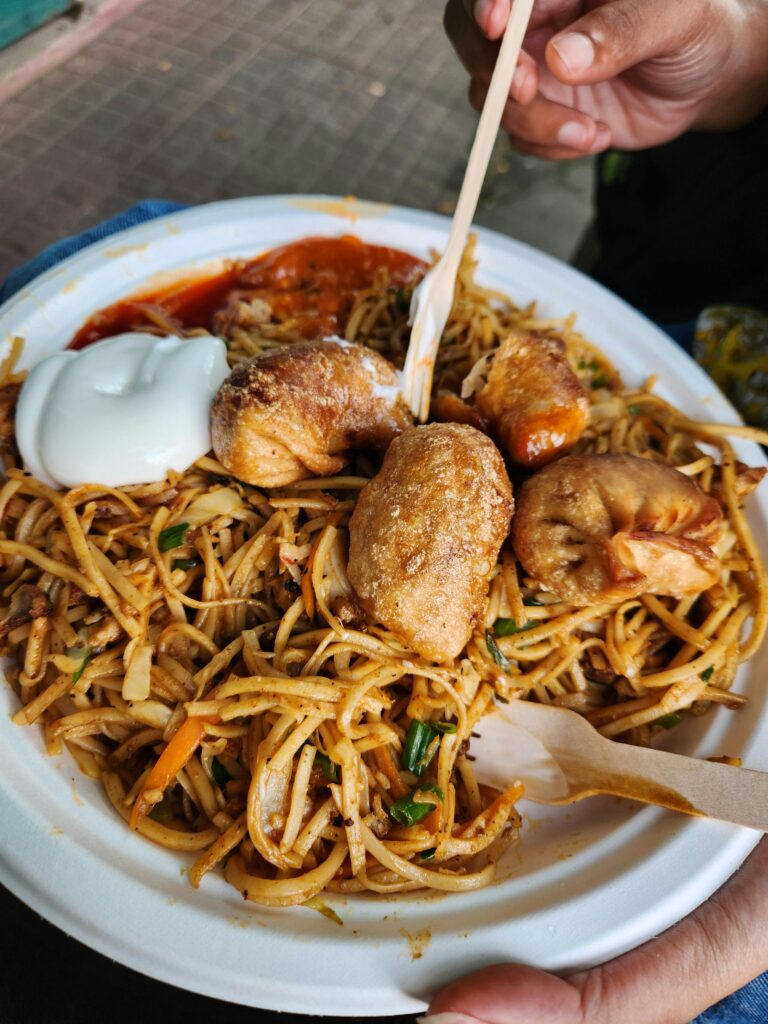 Close-up of a plate filled with noodles and momos, served with sauces, photographed in Ernakulam, India.